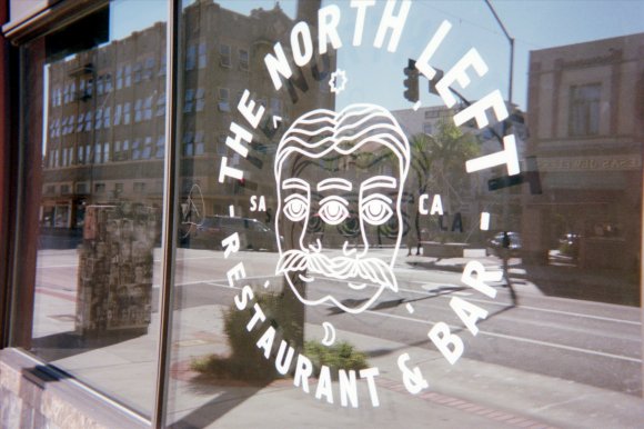 Views of downtown Santa Ana are seen in a reflection in a window for the North Left bar, photographed in September 2014. Digital scan from a Fujifilm 400 disposable camera processed in January 2015.